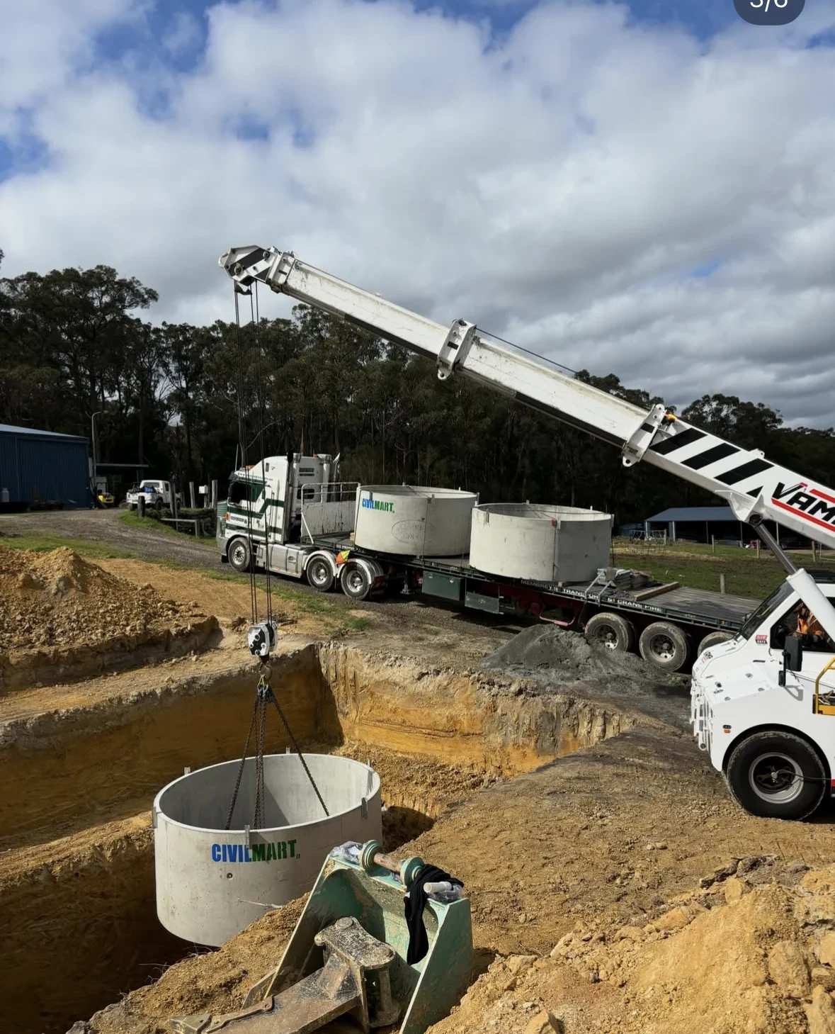 A crane lowering a concrete water tank into the excavation prepared by Barrel